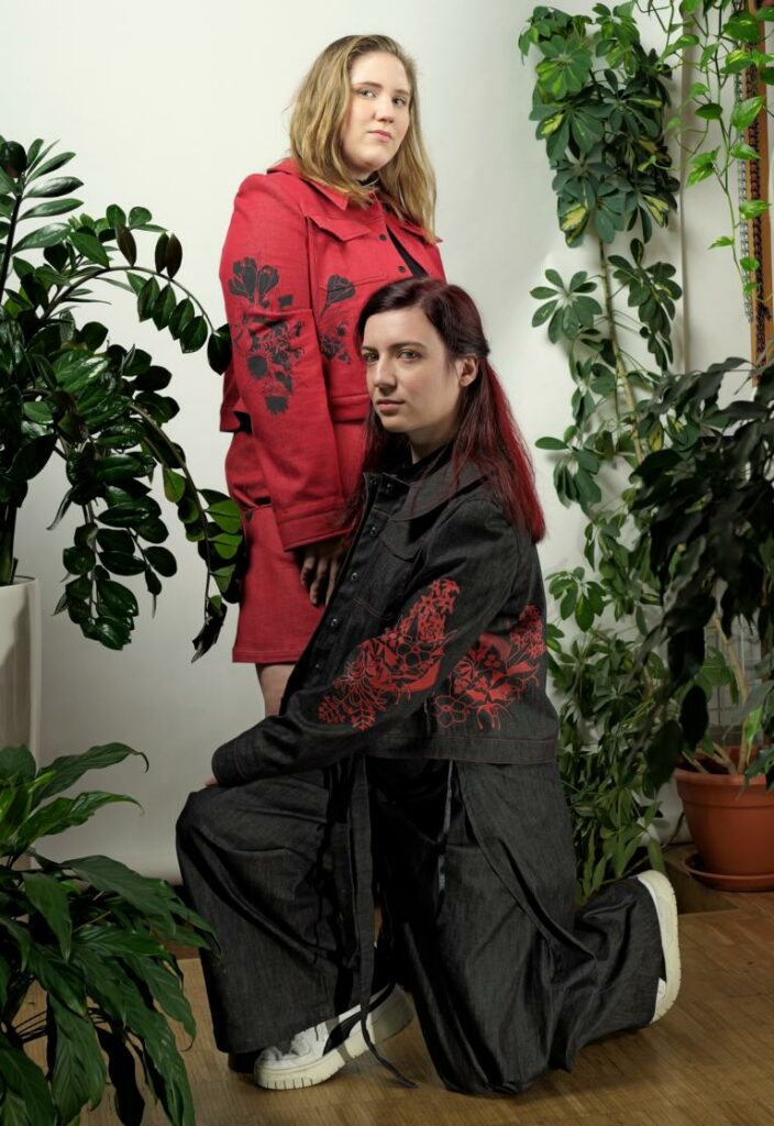 Zwei junge Frauen in Jeansjacken, die mit Blumen bemalt sind; Modedesignerin Evelin Grubbauer und Künstlerin Veronika Hantschel